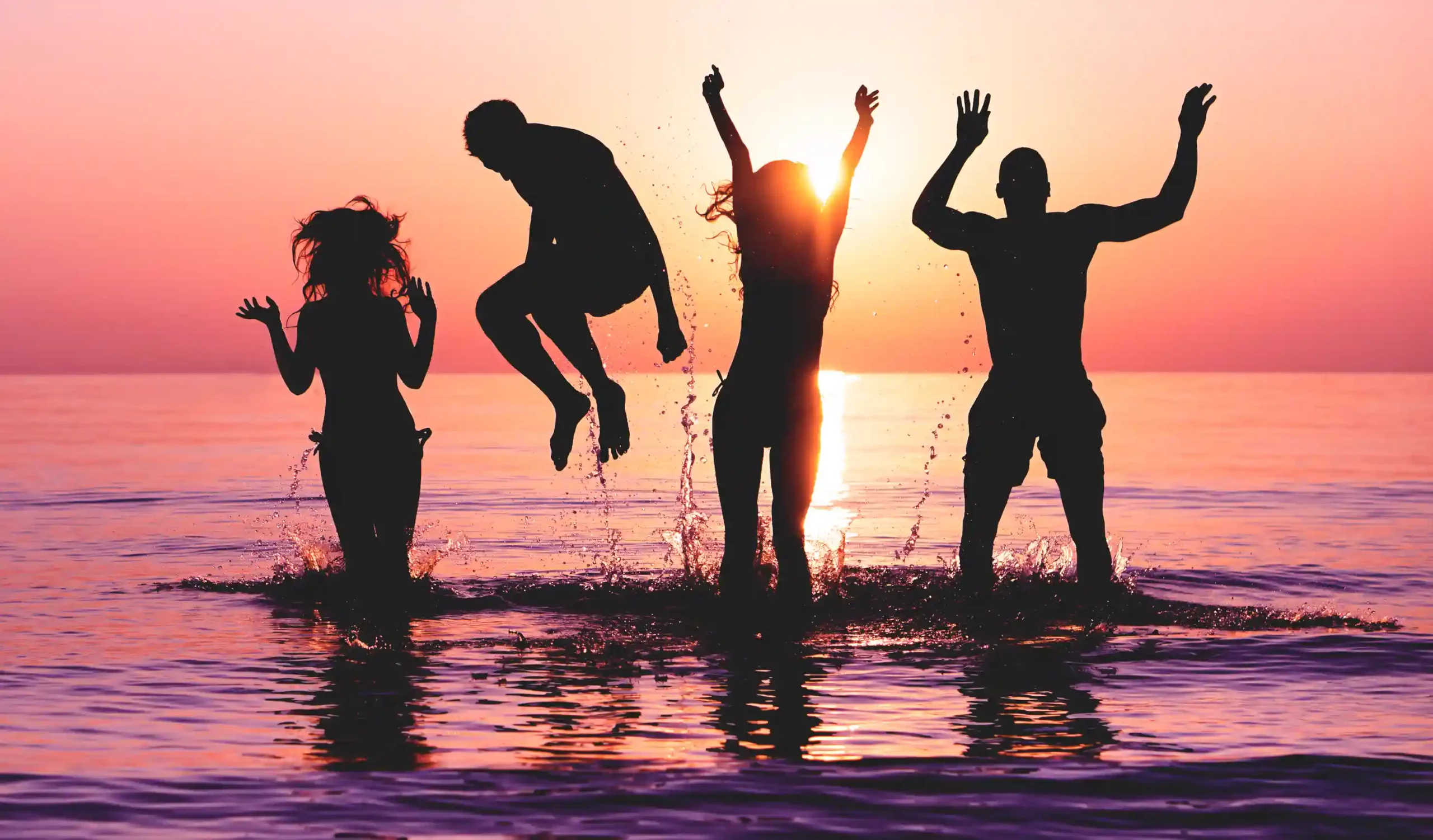 Happy,Friends,Jumping,Inside,Water,On,Tropical,Beach,At,Sunset